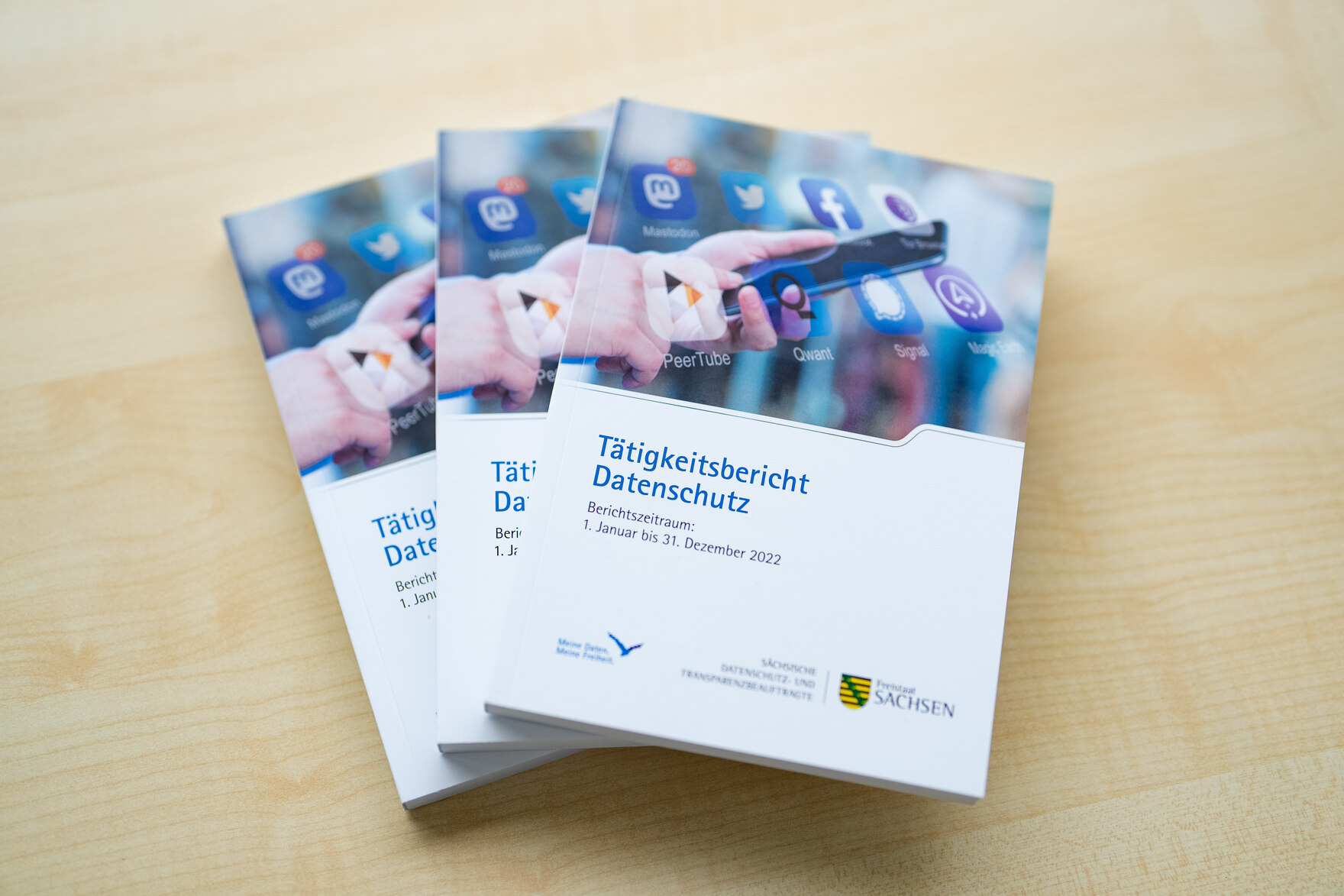 Drei Tätigkeitsberichte der Sächsischen Datenschutz- Transparenzbeauftragten liegen auf einem hellen Holztisch.