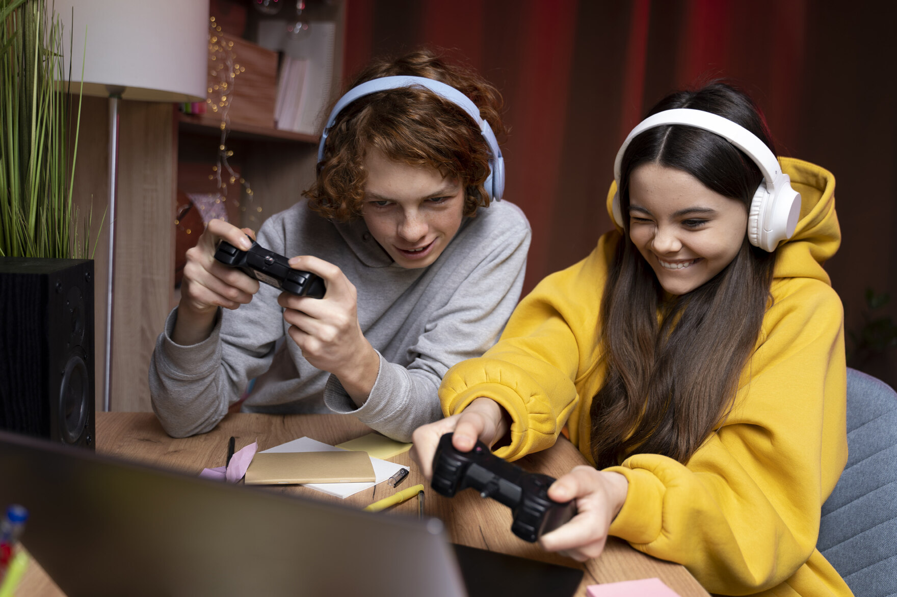 Eine Jugendliche und ein Jugendlicher sitzen vor einem Bildschirm und spielen mit einem Controller ein Videospiel