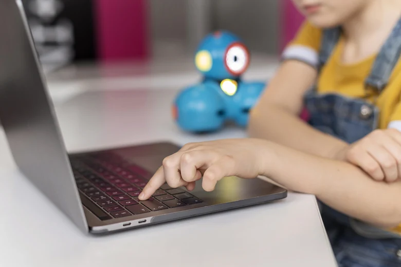 Ein Kind tippt mit dem linken Zeigefinger auf die Tastatur eines Notebooks.