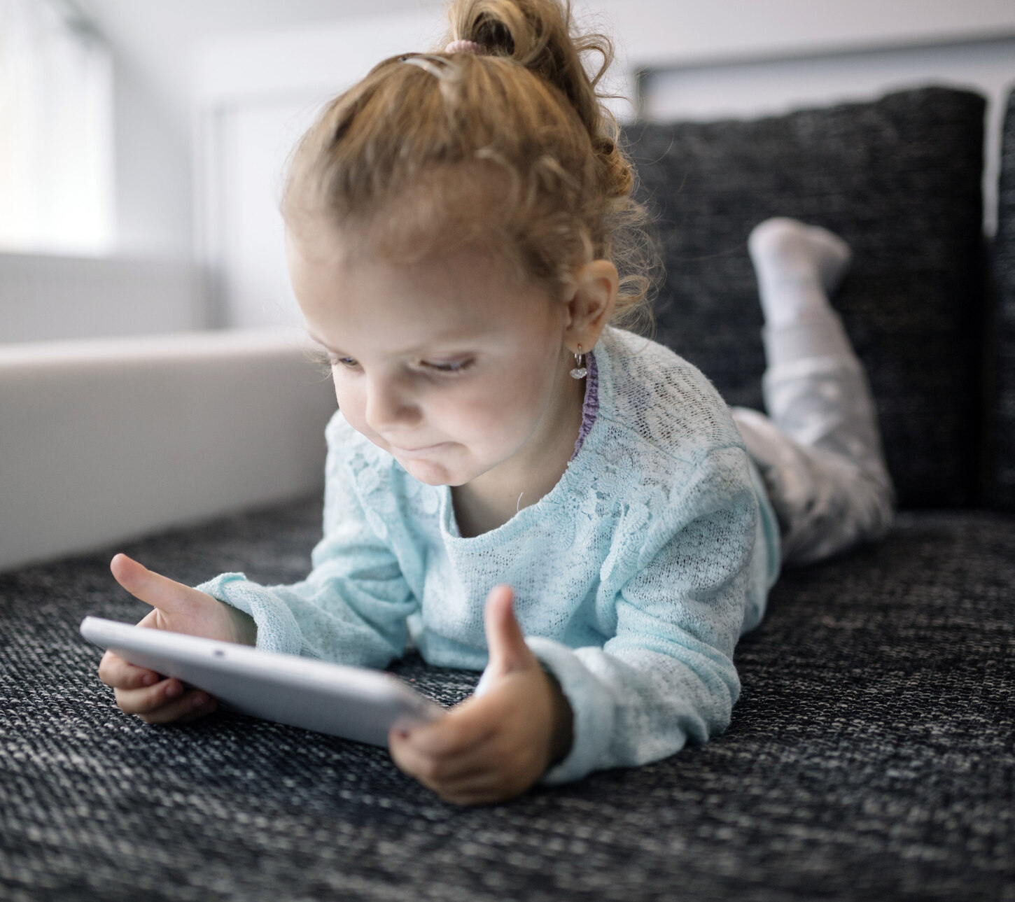 Ein Mädchen liegt auf dem Sofa und hält ein Tablet in der Hand.