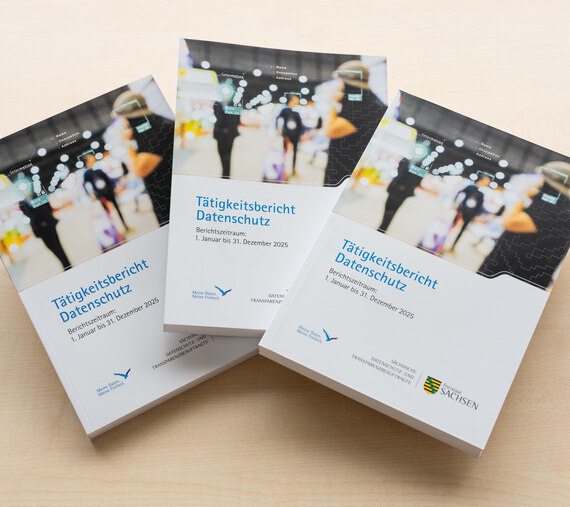 Drei Exemplare des Tätigkeitsberichts Datenschutz 2025 liegen übereinander auf einem hellen Holztisch