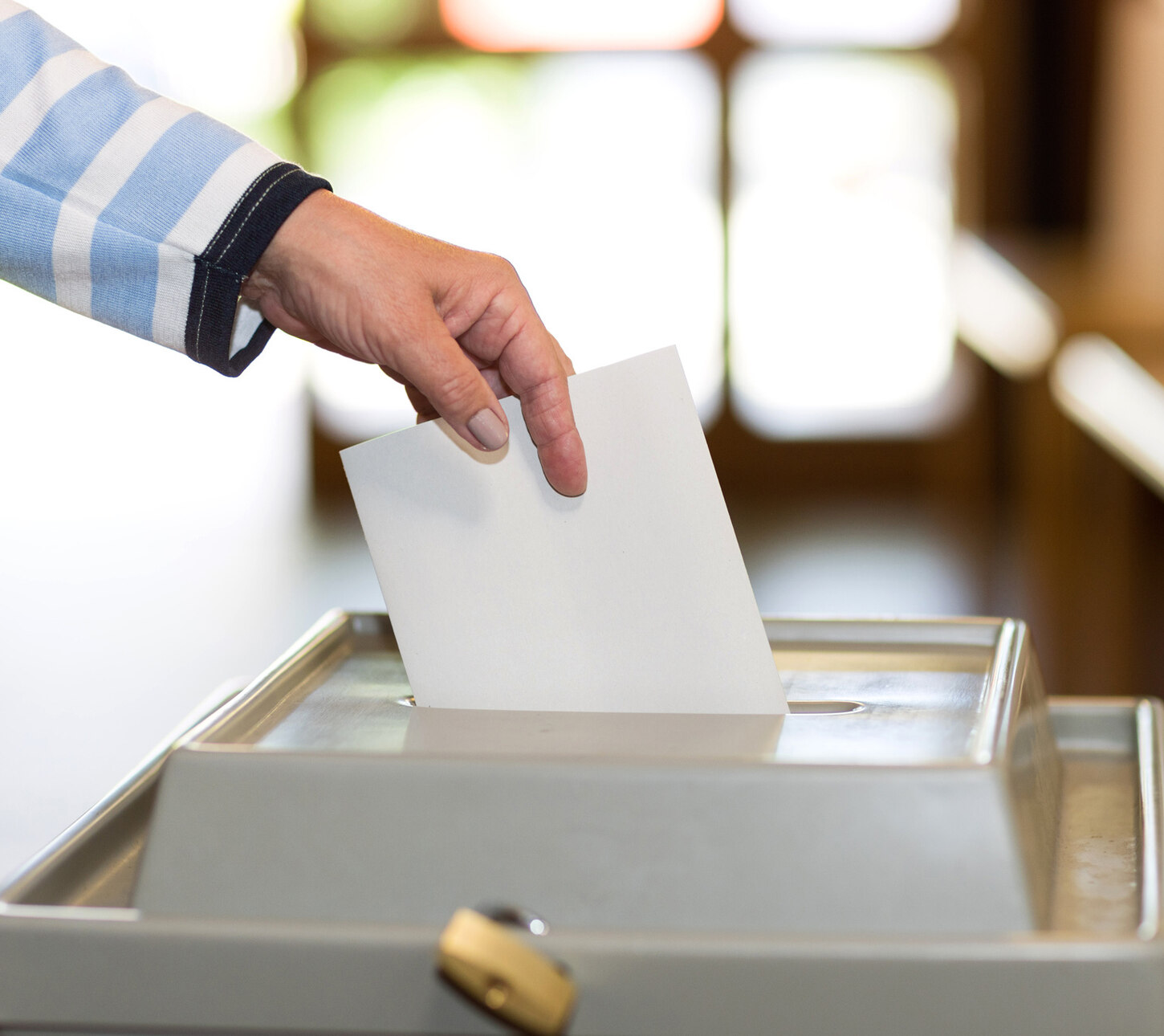 Ein Umschlag wird in eine Wahlurne geworfen.