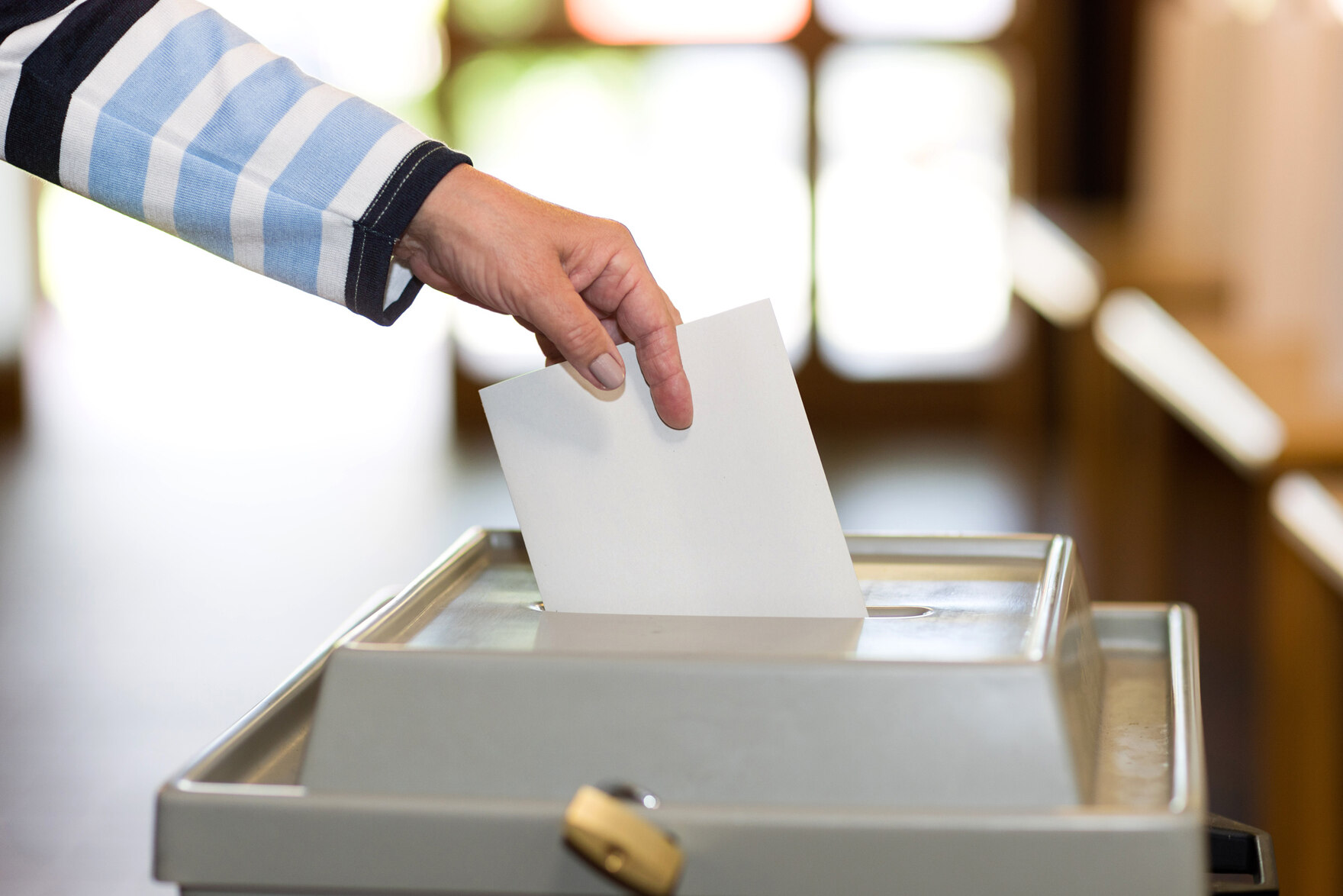 Ein Umschlag wird in eine Wahlurne geworfen.