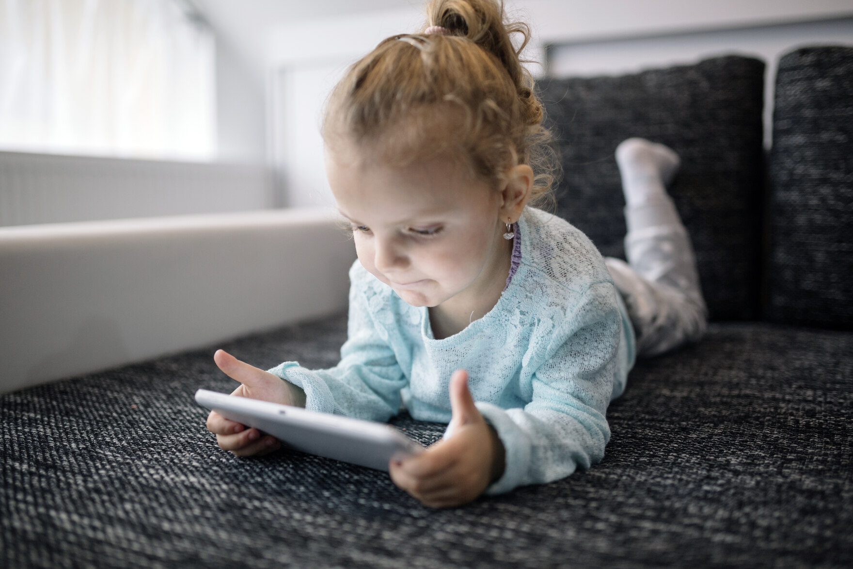 Ein Kind liegt auf dem Sofa und schaut auf ein Tablet.