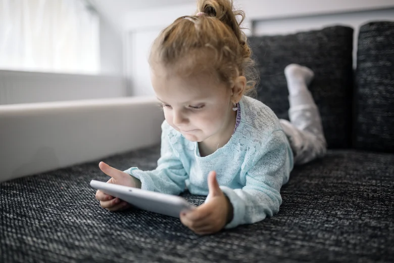 Ein Kind liegt auf dem Sofa und schaut auf ein Tablet.